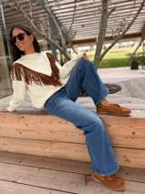 Sweater tejido de lana color negro, con diseño de flecos de gamuza en tono suela aplicados en forma de V en la parte frontal. Presenta cuello redondo y mangas largas.