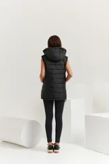 Chaleco negro oversize con capucha forrada en tela gamuzada, cierre metálico YKK, bolsillos laterales y tancas regulables en el ruedo.
