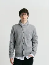 Cardigan de punto color marrón con cuello esmoquin, cierre frontal con botones y presilla superior. Presenta mangas largas con coderas en contraste y bolsillos frontales de ribete.