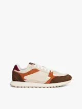 Zapatillas Tommy Hilfiger de estilo retro con paneles de ante y tela en tonos beige, marrón y naranja. Presentan suela gruesa dentada de goma, cierre con cordones y detalles de la marca en la lengüeta y el talón.