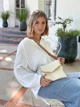 Cartera tipo sobre color crudo, confeccionada en cuero, con correa larga de cuero marrón y costuras decorativas en contraste.