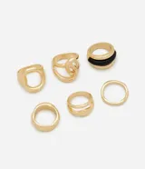 Kit de seis anillos de diseño variado con acabado en tono dorado claro. Incluye piezas de metal con texturas lisas, torcidas y caladas, además de un anillo con detalle de resina negra. Diseñados para ser usados en conjunto o por separado.