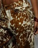 Conjunto de dos piezas con estampado de vaca en tonos marrón y blanco. Incluye un top sin mangas con cuello alto y cierre frontal mediante cordones cruzados, y un pantalón de corte holgado a juego.