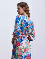 Vestido midi con estampado floral en tonos azules, rojos y blancos. Tiene escote en V, mangas 3/4 con puños fruncidos, cintura elastizada con lazo de ajuste y falda con volantes.