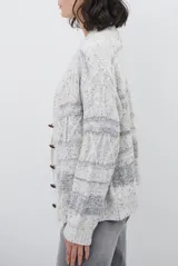 Sacon de tejido de punto grueso con diseño de ochos y rayas horizontales en contraste. Presenta cuello en V, cierre frontal con botones oscuros y mangas largas con puños acanalados.