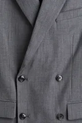 Blazer cruzado de color gris medio, con solapas de pico, ojal decorativo y cierre de doble botonadura. Presenta bolsillo superior insertado, bolsillos delanteros ribeteados con solapa y botones decorativos en los puños.