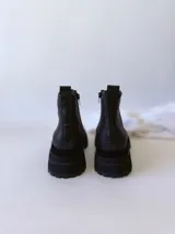 Botas negras de cuero con caña baja, cierre lateral con cremallera y suela track.