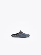 Zapato destalonado tipo slide color azul con diseño de micromotivo geomético, combinado con detalles de cordones y apliques de cuero marrón, ojales metálicos y un pasador metálico decorativo en el lateral.