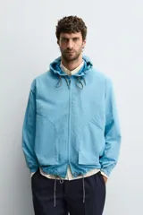 Cazadora técnica ligera de corte regular, con capucha ajustable, cierre frontal con cremallera y puños elásticos. Presenta bolsillos tipo plastrón en la parte frontal y bajo ajustable con cordón.