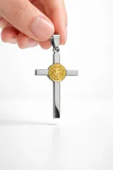 Dije en forma de cruz de acero inoxidable plateado con medalla central dorada de San Benito.