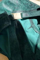 Falda corta de cuero ovino color verde azulado con efecto vintage, corte irregular y aberturas laterales con lazos.