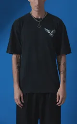 Remera de manga corta con cuello redondo y calce oversize, confeccionada en algodón premium con efecto de lavado nevado. Presenta una estampa gráfica en la espalda con diseño de palomas y texto alusivo.