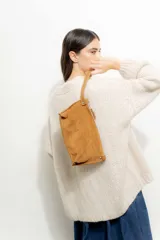 Sobre de mano tipo clutch confeccionado en cuero agamuzado color tostado, con cierre superior y correa de muñeca integrada.