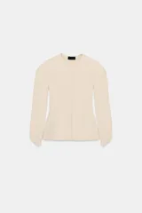 Chaqueta de punto color crema, con cuello redondo, manga larga abullonada en el hombro y acabado asimétrico en el puño. Cierre frontal con botones.