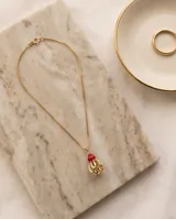 Collar de cadena fina dorada con dije de bronce que combina una piedra roja superior y una estructura esferoide inferior texturizada y calada.