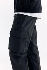Pantalón cargo negro de nylon, de corte regular con cintura elástica ajustable con cordón. Cuenta con bolsillos laterales con cierre, bolsillos cargo con solapa en las piernas, bolsillos traseros con cierre y tensores en los tobillos.
