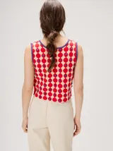 Top de punto sin mangas con escote en V, cierre frontal con botones y estampa geométrica de círculos rojos sobre fondo beige, con detalles en color violeta y apliques en relieve.