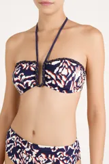Top de bikini bandeau con aro en U en el centro y tiras halter que se atan al cuello. Presenta un estampado abstracto en tonos azules, blancos y naranjas, con detalles de cordones trenzados y flecos colgantes en los breteles.