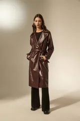 Trinchera de eco-cuero en color bordó, con diseño de doble botonadura, solapas amplias y cinturón ajustable en la cintura. Presenta mangas largas con detalles en los puños y bolsillos laterales.