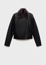 Chaqueta estilo biker de efecto piel en color negro, con cuello y forro interior de pelo sintético en tono gris oscuro. Presenta cierre frontal de cremallera, manga larga y diseño estructurado.