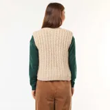 Chaleco de punto beige con textura de ochos, sin mangas, con cuello redondo y cierre frontal con botones grandes dorados.
