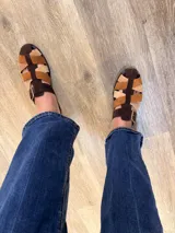 Sandalias estilo sueco confeccionadas en cuero con tiras entrelazadas de gamuza en tonos marrón, tostado y beige, con hebilla metálica lateral.