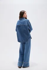 Sobrecamisa de jean azul medio, de corte oversize, con mangas largas y detalles de tachas decorativas en la parte frontal y trasera.