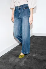 Jeans de tiro alto con corte culotte y pernera ancha. Presenta bolsillos de plastrón en el frente con detalle de pespuntes decorativos en forma de onda y costuras verticales a lo largo de la pierna. Cierre frontal con cremallera y botón metálico.