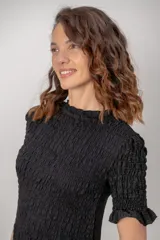 Vestido corto de color negro, con cuerpo y mangas cortas de nido de abeja fruncido, y falda corta con vuelo.