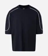 Remera de algodón color blanco, con cuello redondo, manga corta y detalle de raya negra contrastante que recorre la parte superior de los hombros y mangas. Diseño de corte holgado.