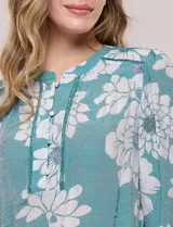 Blusa de gasa texturizada color verde con estampado floral blanco, cuello mao con escote en V y botones frontales. Cuenta con mangas 3/4 abullonadas y detalles de puntilla calada en el pecho.