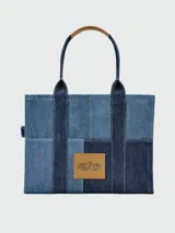 Cartera tote bag Marc Jacobs modelo The Traveler Tote, confeccionada en denim azul con el nombre de la marca estampado en el frente. Cuenta con doble asa superior.