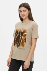 Remera de algodón color beige, de manga corta, cuello redondo y corte holgado. Presenta un estampado frontal con efecto foil metálico dorado y la inscripción "INSPIRATION".