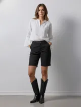 Bermuda de jean color negro, con cierre frontal y botón, bolsillos laterales y diseño clásico de cinco bolsillos.