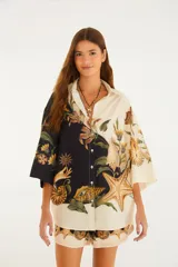 Camisa holgada de algodón con diseño bicolor (mitad negra y mitad cruda) y estampado surrealista de conchas marinas, estrellas de mar y elementos botánicos. Cuenta con cuello camisero, cierre frontal de botones y mangas anchas.