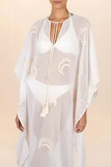 Kaftán largo de algodón traslúcido color blanco marfil, con bordados en tono beige claro en el frente y en los bordes. Presenta un escote en V con cordones terminados en borlas.