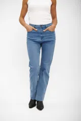 Jean de corte recto y tiro medio, color azul medio, con diseño clásico de cinco bolsillos y ruedo deshilachado.