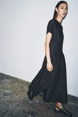 Vestido midi de denim color negro con cuello redondo y manga corta. Presenta un diseño con cintura entallada tipo bustier y falda con corte evasé. Cierre posterior con cremallera.