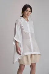 Camisa blanca de lino con cuello clásico, cierre frontal con botones, mangas anchas 3/4 y detalles de bordado calado en el canesú y los puños.