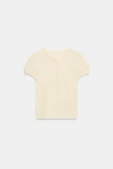 Camiseta color amarillo claro de 100% algodón, con cuello redondo, cierre frontal de botones tipo panadero y mangas cortas abullonadas.