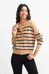 Sweater de tejido de punto color beige con rayas horizontales negras. Presenta cuello polo con abertura frontal abotonada con tres botones marrones.