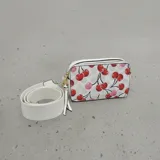 Cartera tipo bandolera de formato rectangular con estampado de cerezas sobre fondo claro. Cuenta con cierre superior, tirador con flecos y correa de tela ajustable y extraíble.