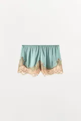 Shorts de satén color turquesa con cintura elástica y bajo decorado con aplicación de encaje en tono contrastante.