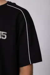 Remera de algodón color blanco con corte regular, cuello redondo y mangas cortas. Presenta detalles de líneas finas negras en los hombros y estampado gráfico frontal con tipografía y logotipos en color negro.