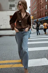 Camisa marrón de manga larga con cuello solapa y cierre frontal de botones. Los puños terminan con lazos anudados.