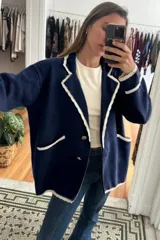 Blazer tejido de punto en color azul marino con detalles de bordes en color crema. Presenta solapas con diseño ondulado, cierre frontal con botones dorados y bolsillos laterales con ribete en contraste.