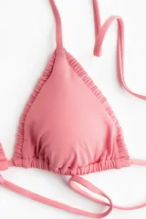 Top de bikini triangular color rosado con relleno extraíble, tiras para anudar al cuello y la espalda, y detalle fruncido en los bordes.