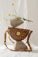 Bandolera de cuero con forma de media luna y estampado animal print. Cuenta con cierre superior, herrajes metálicos dorados y correa regulable para llevar al hombro o cruzada.