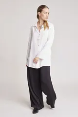 Camisa blanca de satén con cuello clásico, cierre frontal con botones y mangas largas.