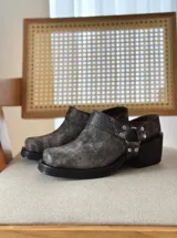 Zueco de cuero con efecto desgastado en tono visón, con diseño de punta cuadrada, suela gruesa negra y detalle de correa con tachas metálicas y argolla lateral.
